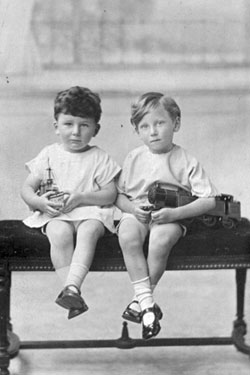 Portrait of two children seated. (They appear to be holding toy boats). 	
